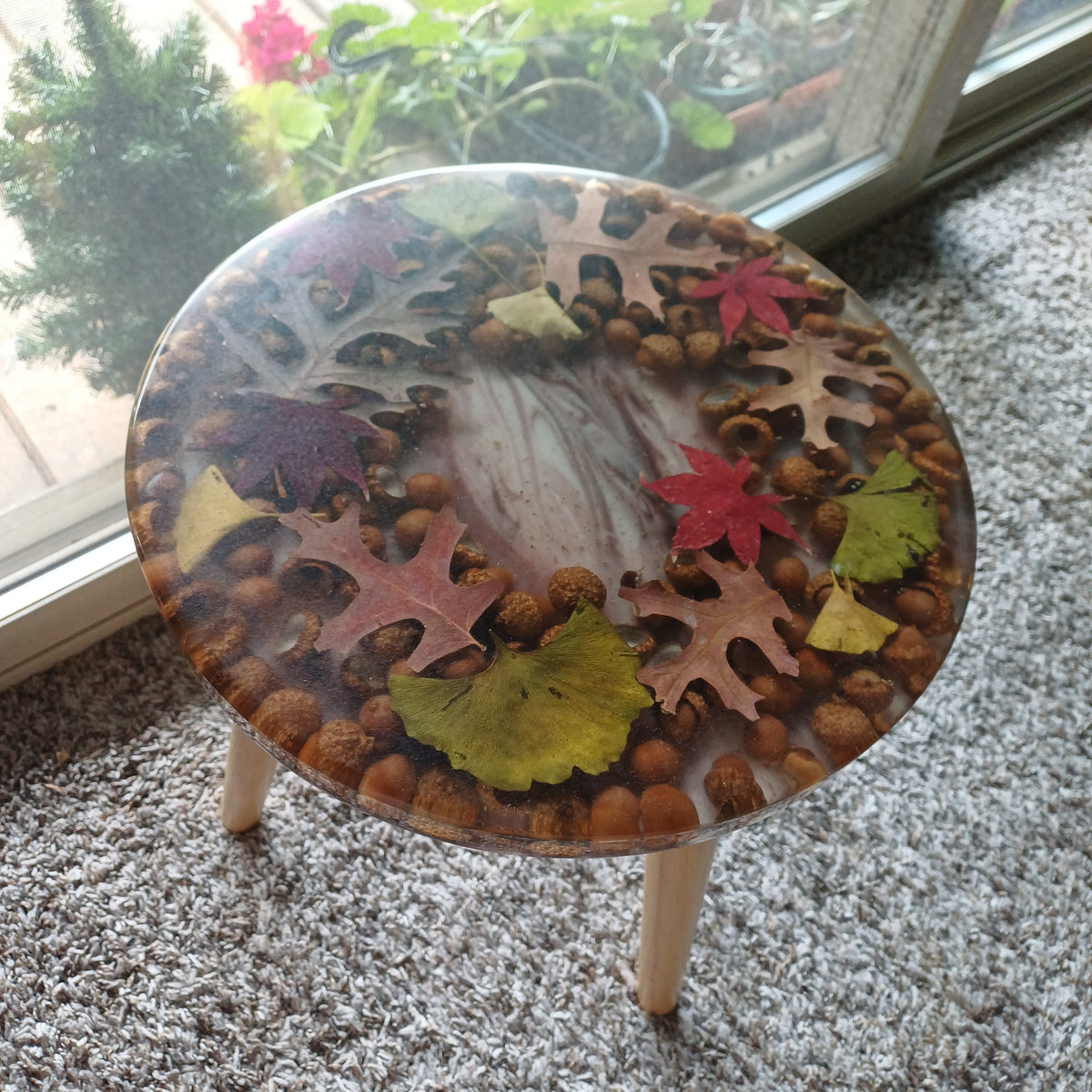 Round handmade resin side table with real oak, maple and ginkgo leaves and acorns under a clear epoxy top, wooden legs